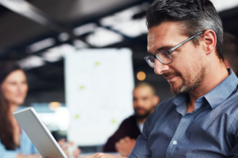 A man with glasses using a tablet in an office environment.