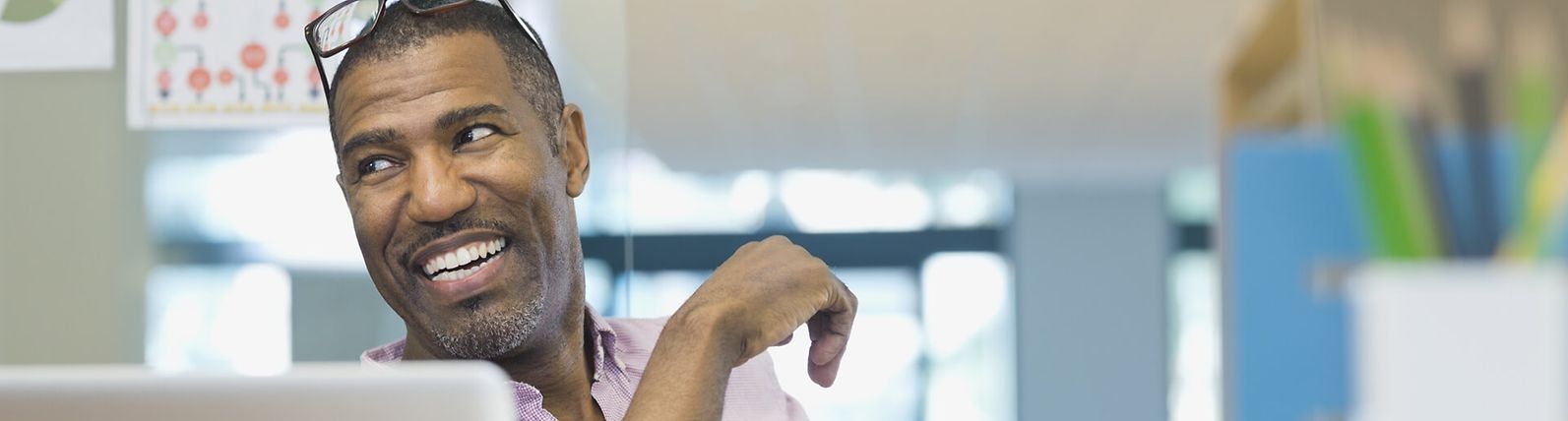 Businessman sitting at a desk, smiling, with glasses on his head.