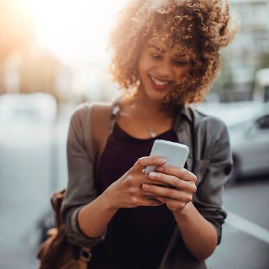 Young woman using smartphone, walking outdoors, smiling.