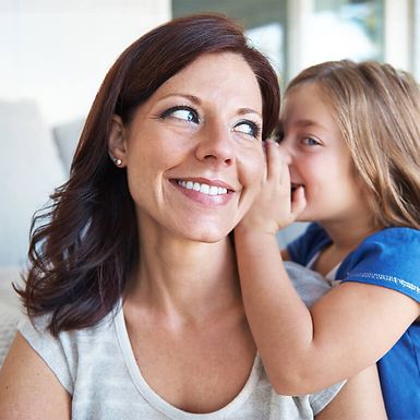 A young girl whispering in her mother's ear
